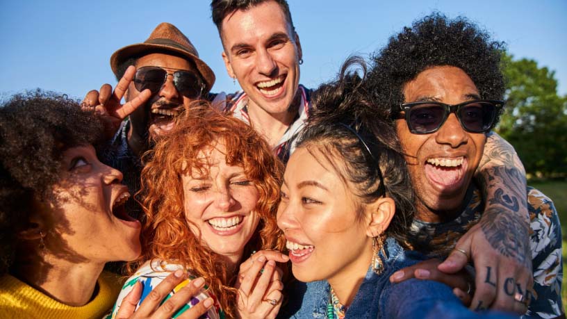 A group of friends embrace each other as they pose for a photo on a sunny day.