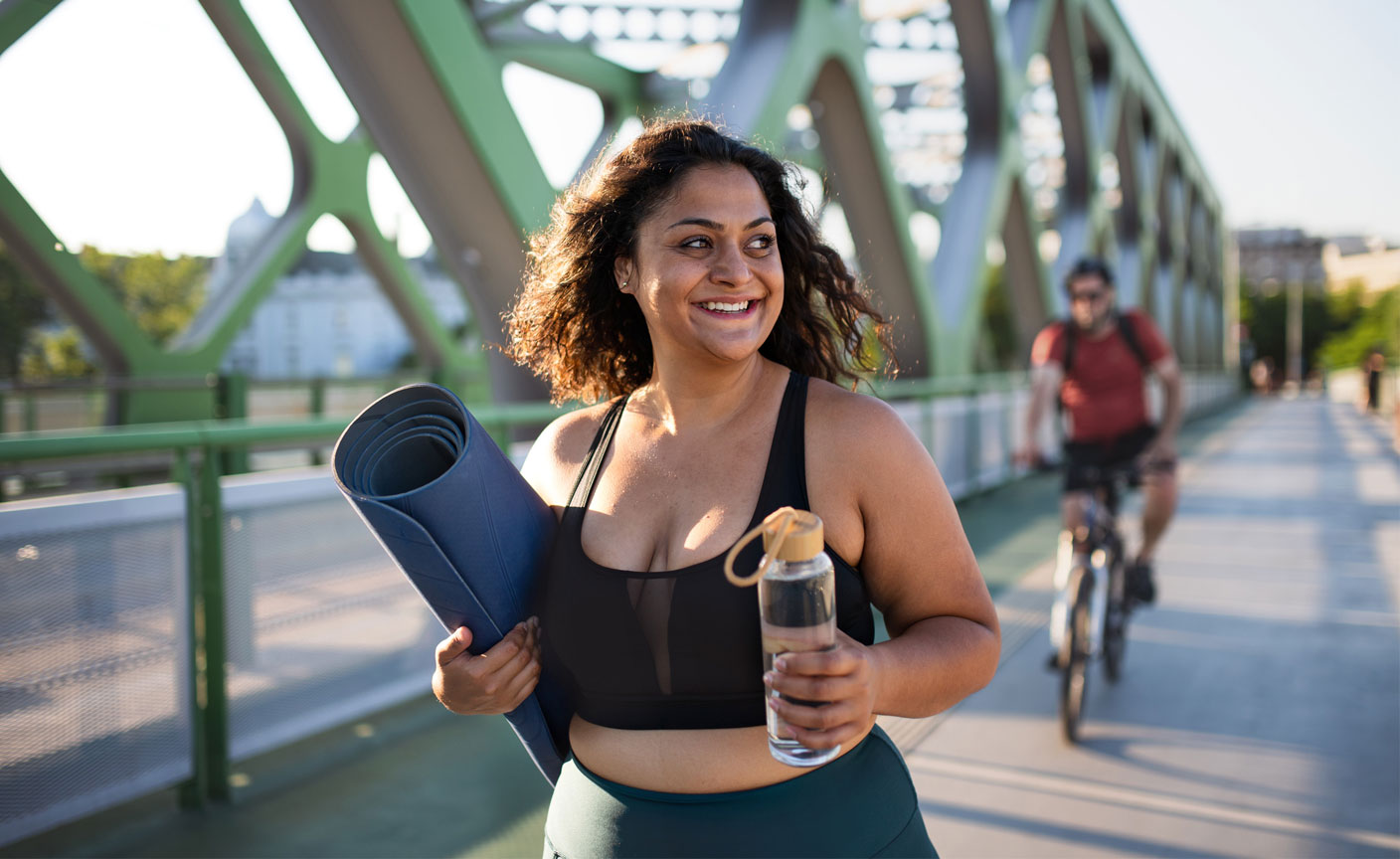 Smiling woman walking with fitness mat and water bottle