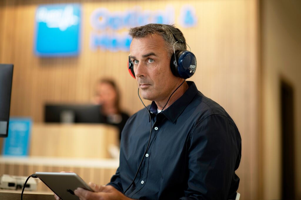 Man at Bupa clinic with headphones in his ears and ipad in hands