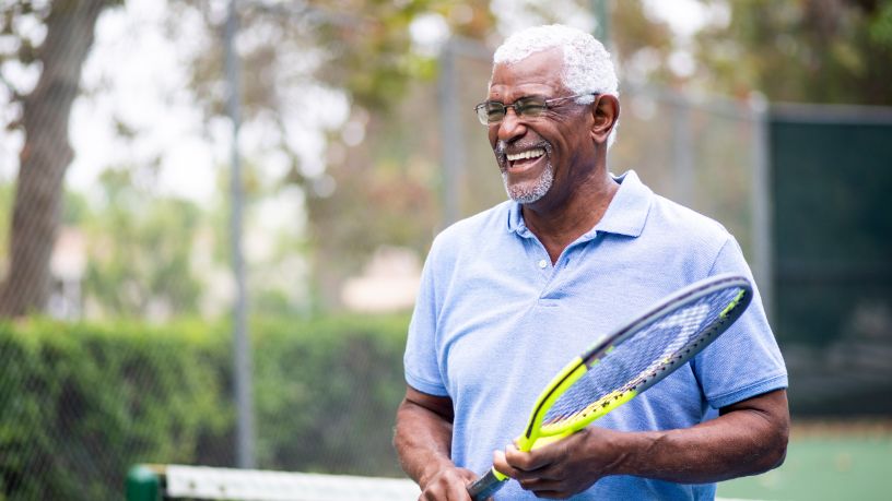 Man smiling widely while holding a tennis racket.