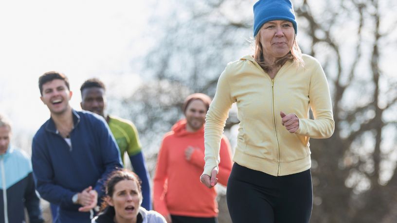 A woman runs while a group of people stand behind her, cheering her on.
