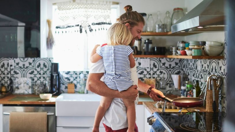A man holding baby and putting pan on the stovetop in a kitchen.