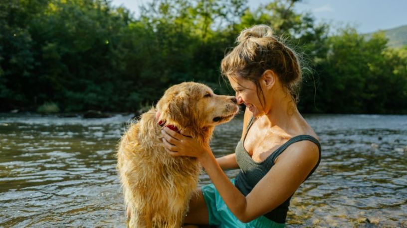 A woman and dog touch noses next to a river.