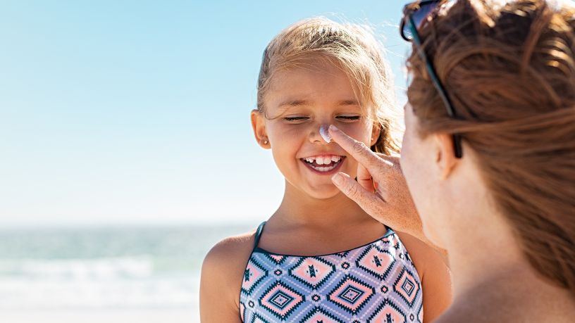 A woman applies sunscreen to her daughter's nose at the beach.
