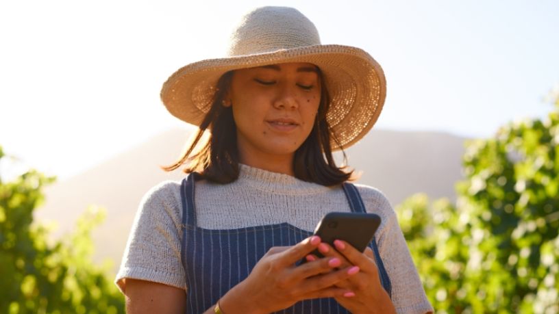 Woman outside in a wide brimmed hat looks at her phone.