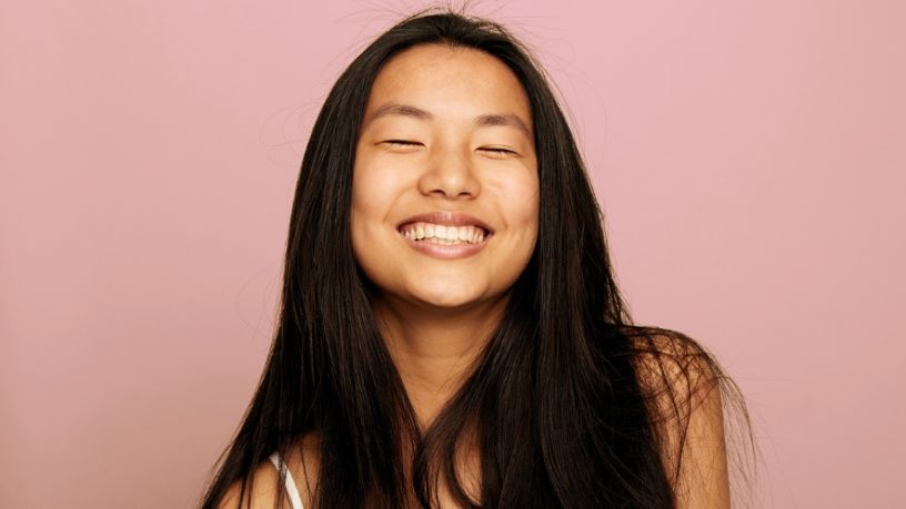 Young woman with long dark hair smiling with her eyes closed.