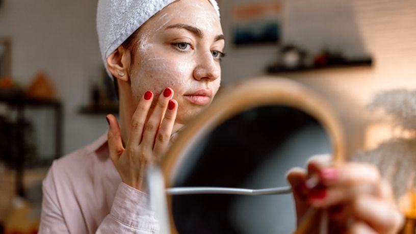 Woman applies face cream in a hand mirror