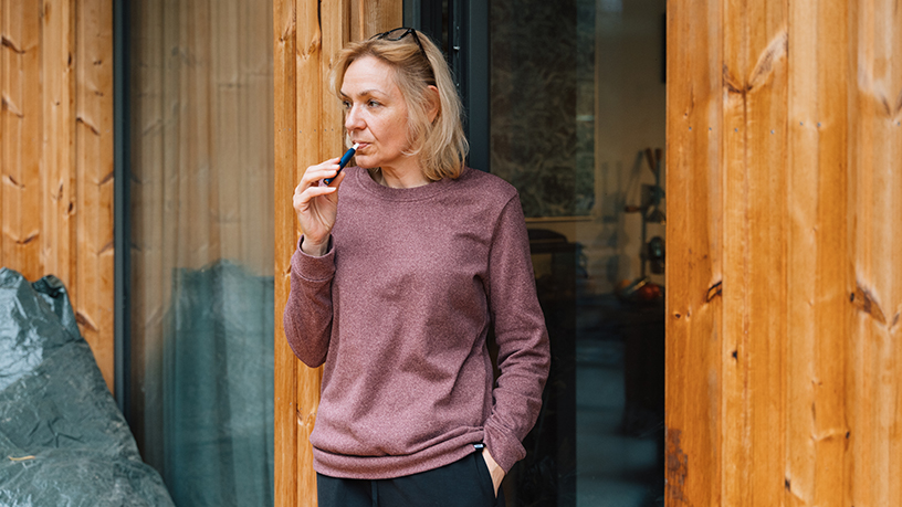 A woman standing outdoors vaping.