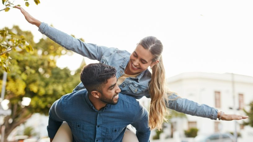 A man gives a woman a piggyback as she holds her arms out like and airplane