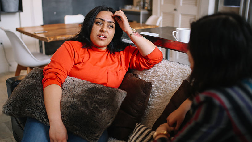 Two friends sitting on the coach talking.
