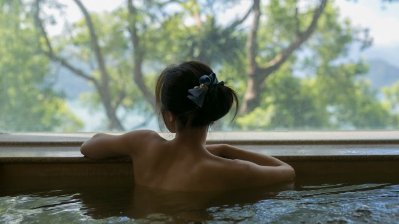 A woman looks out over trees from a natural pool.