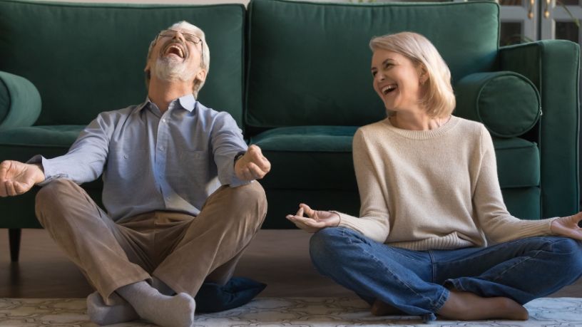 A man and a woman laugh as they sit on the floor and meditate.