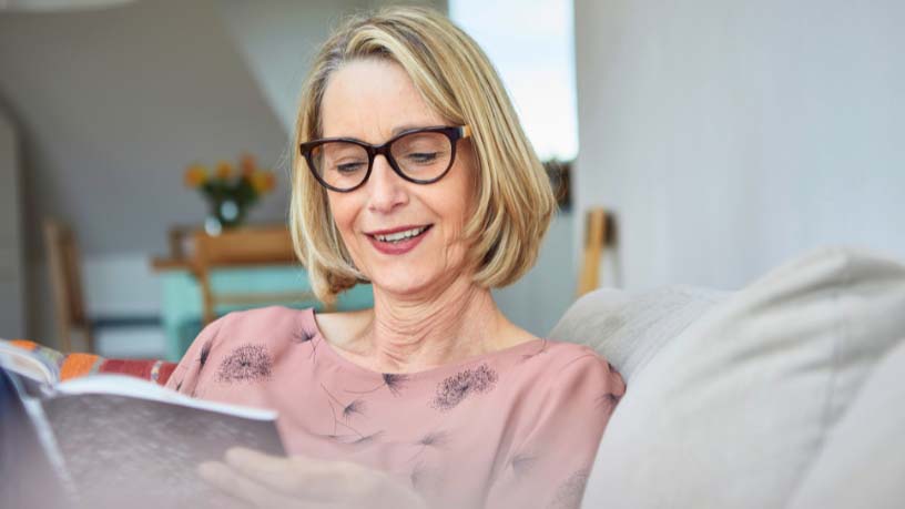 A woman sits on her couch writing in her diary.