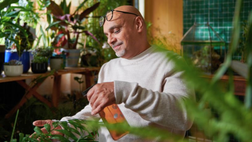 A man relaxes while spraying water on his plants.
