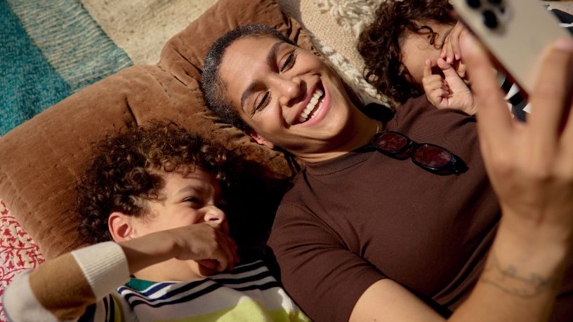 A parent lies on a couch with two kids, looking at a phone.