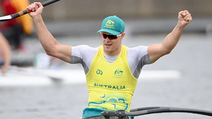 Paralympian Curtis McGrath in a yellow Australian competition singlet raises his arms in a "V" for victory while competing on the water.