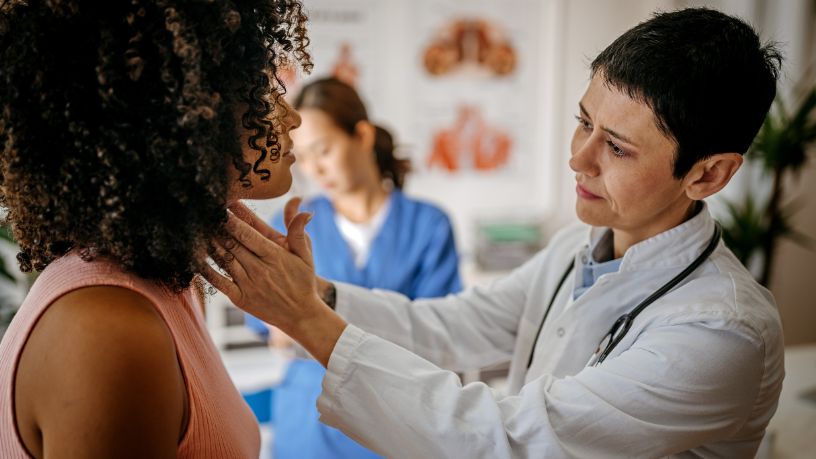 A doctor checks a woman's throat by gently pressing on it.