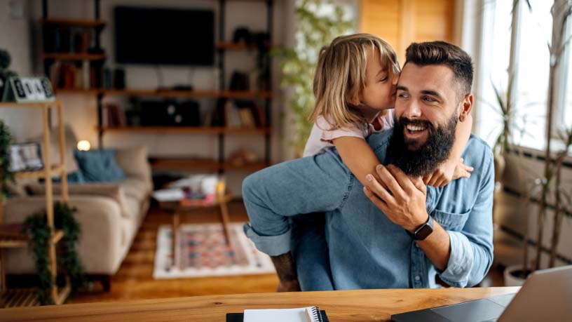 A girl hugs her dad over his shoulders.