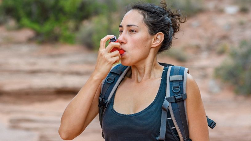 A hiker pauses on a rocky trail to use her inhaler.