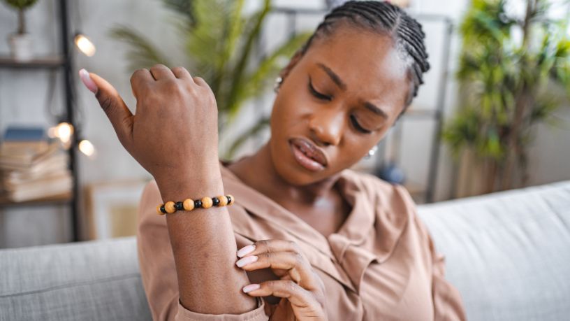 A woman grimaces while looking at an itchy spot on her arm.