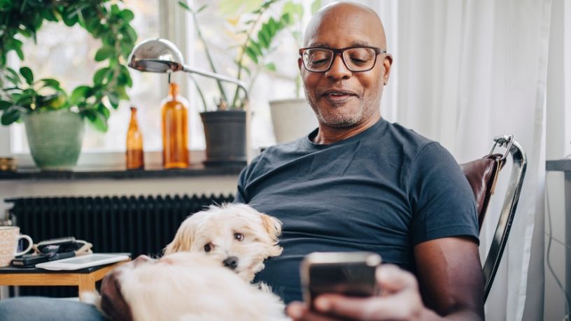 A man sits with his dog on his lap while looking at his phone.