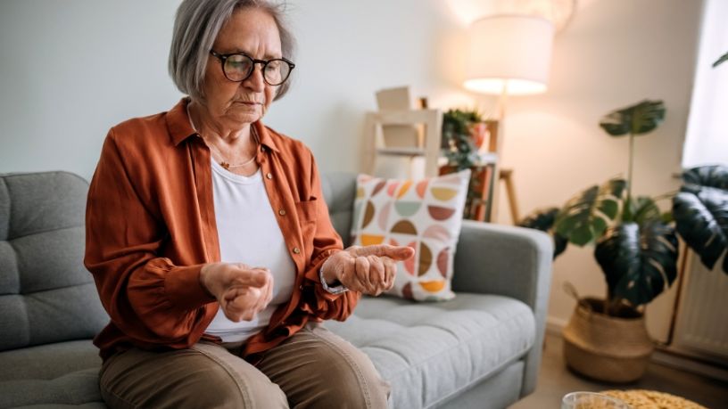 A woman sits on a couch checking her wrists.
