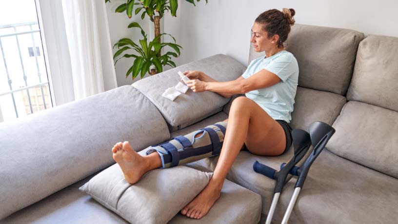 A woman lying on a couch and applies new bandages to her injured knee.