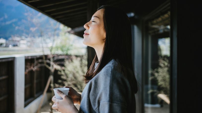 A woman relaxes with a coffee on her balcony.