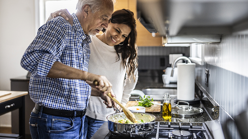 A woman and her father cooking together.