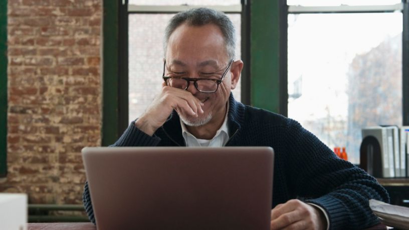 A man smiles while looking at his laptop.