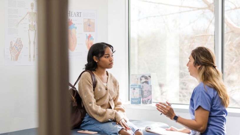 Woman sitting on a hospital bed talking to her care team.