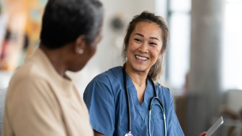 A doctor holds a clipboard and smiles as she talks with a patient.