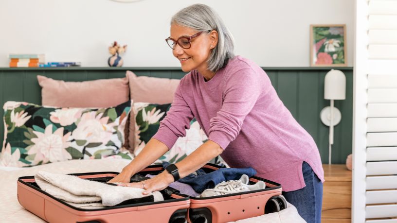 A woman smiles as she backs a small suitcase with clothes.