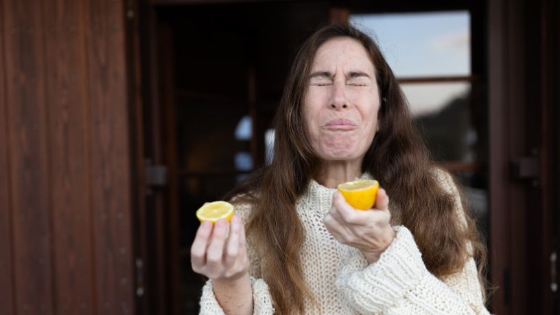 A young woman biting into half a lemon and making a funny face.