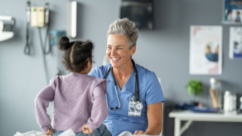 A medical professional smiling and talking to a young child in clinic.
