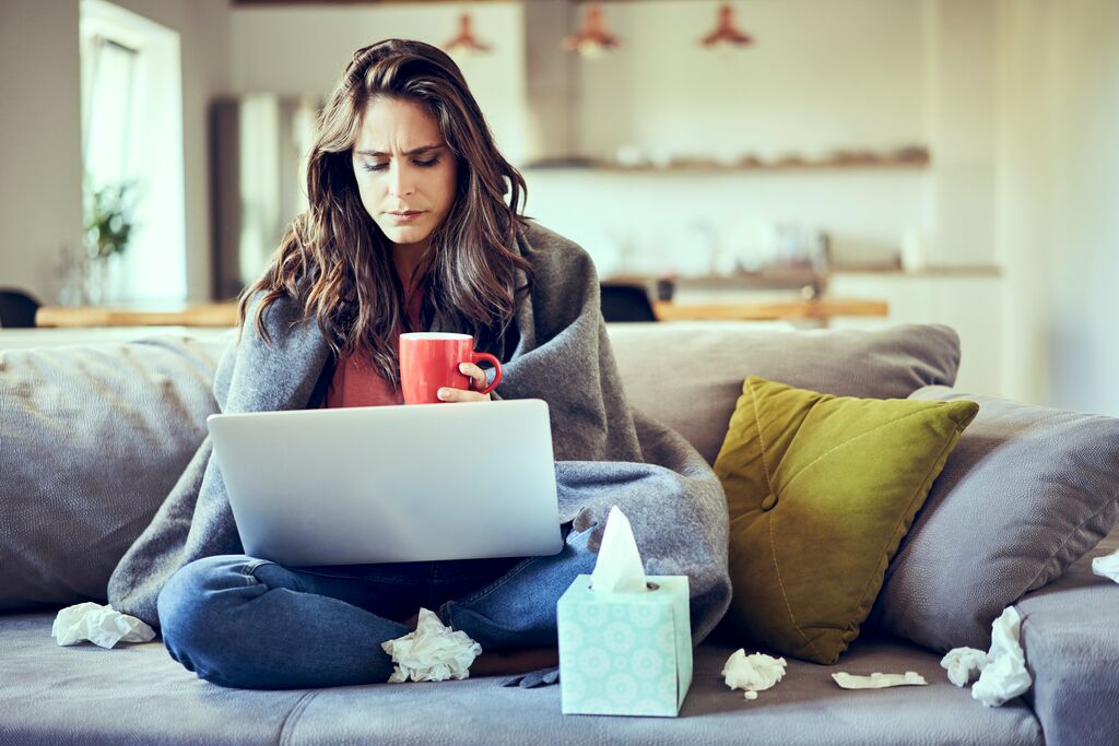 A woman sitting on the couch with her computer, with a cold.