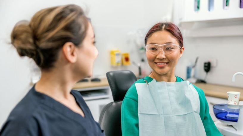 A patient in a dentist’s office smiles at a dental health professional.