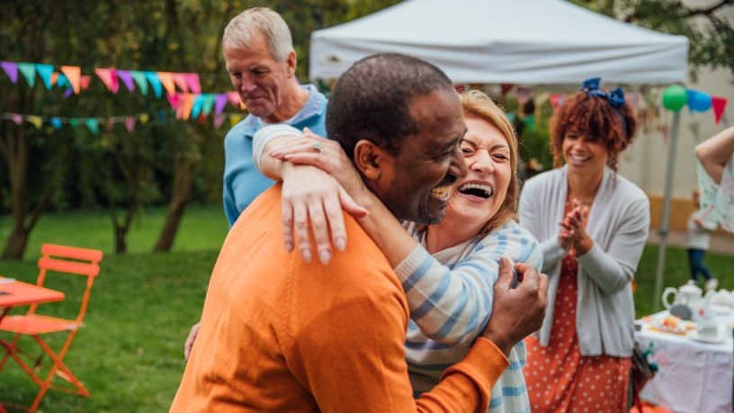 Two friends laugh and hug at a backyard party.