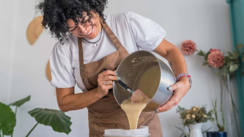 A chef pours cake batter from a mixing bowl into a lined cake pan.