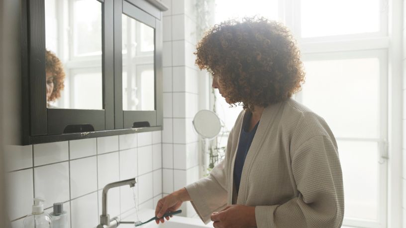 A woman standing in the mirror brushing her teeth.