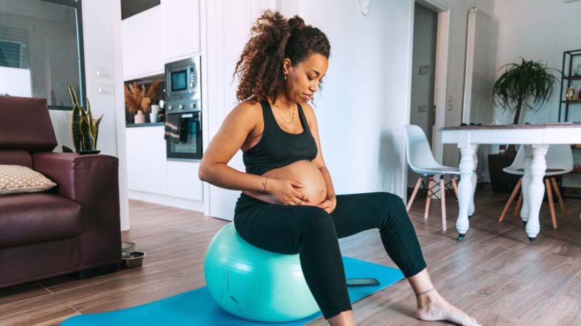 A woman on an exercise ball cradles her pregnant belly.