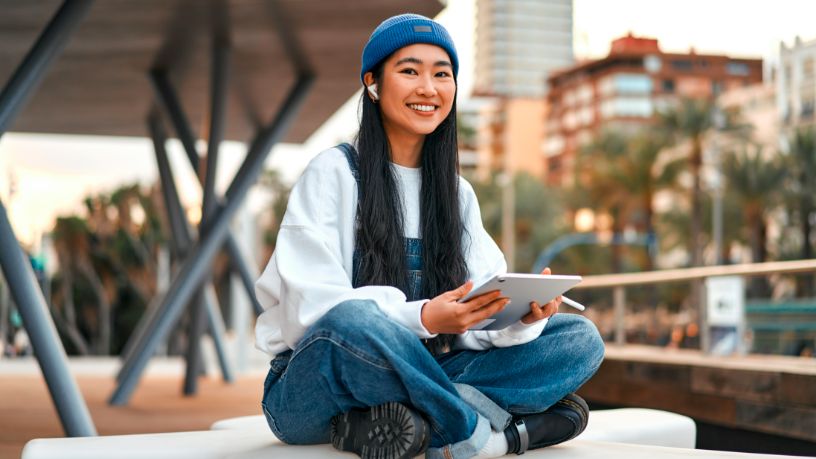 A woman sits outside with her headphones in and smiles.