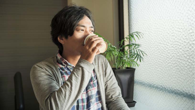 A man stands by a window drinking from a cup.