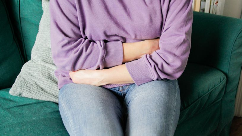 A woman sitting on a couch holds her stomach.