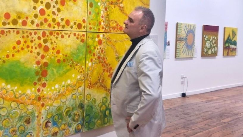 Murray stands in a gallery looking at his painting. It takes up an entire wall.