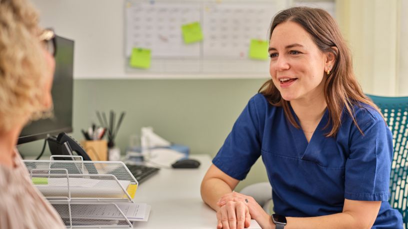 A doctor speaks with her patient at her desk.