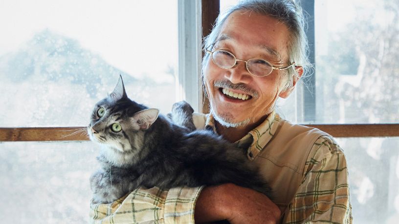 An older man smiles while holding his cat.