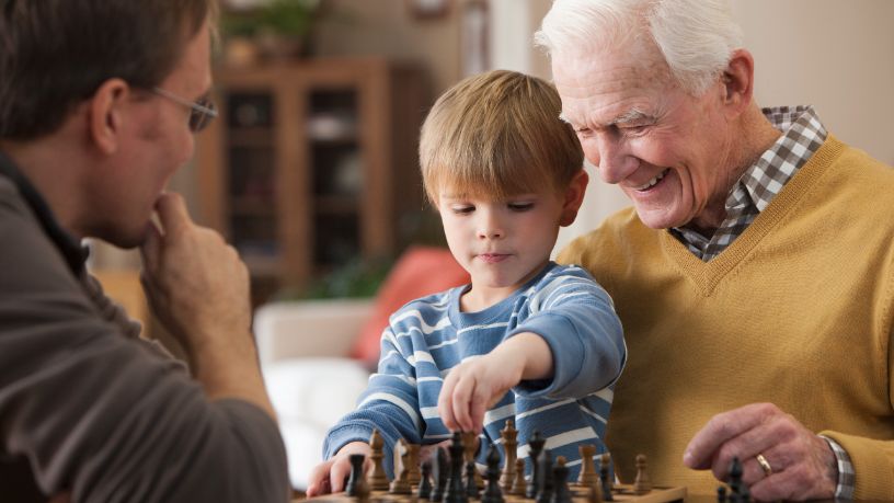 A man plays chess with his young grandson.