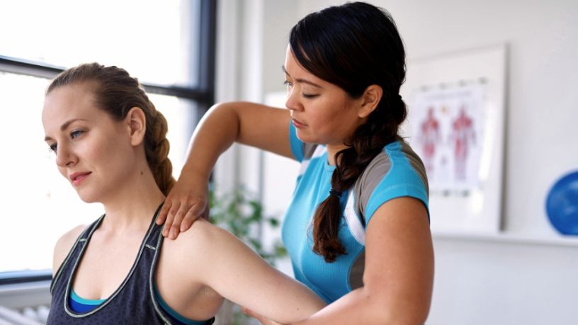 A physiotherapist adjusts her patient’s shoulder in a treatment room.