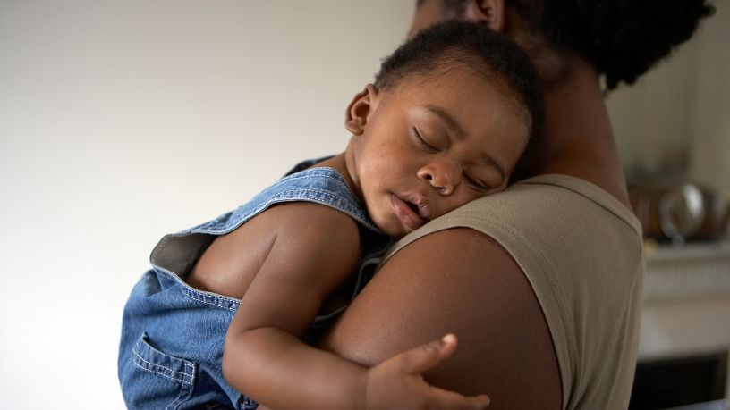 A woman holds her sleeping baby to her shoulder.